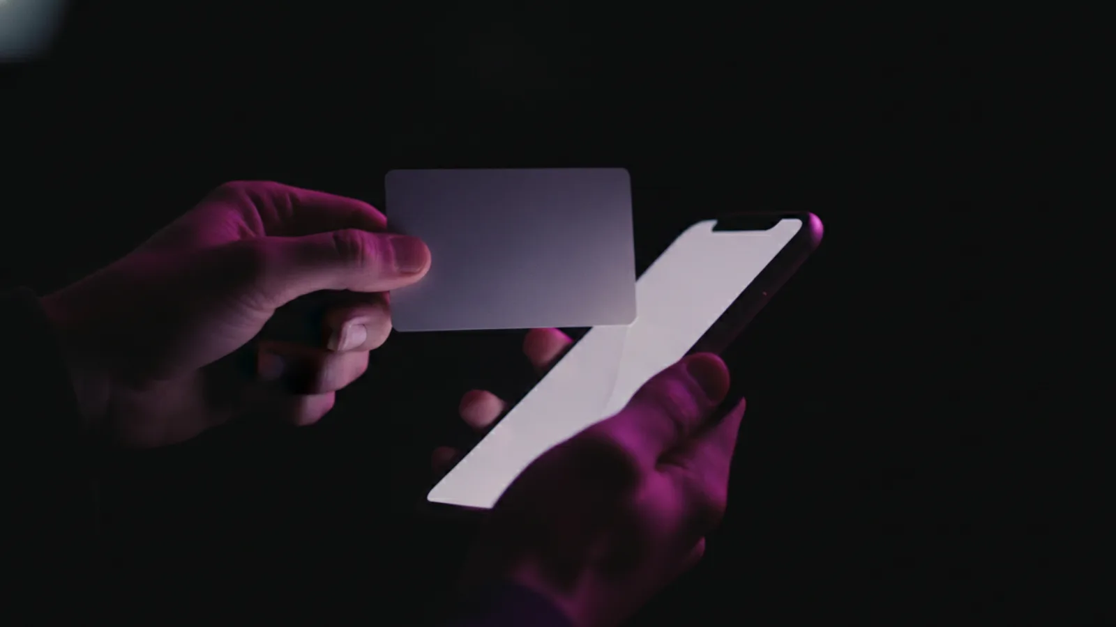 A hand pulling a bank card away from a smartphone in a dark room