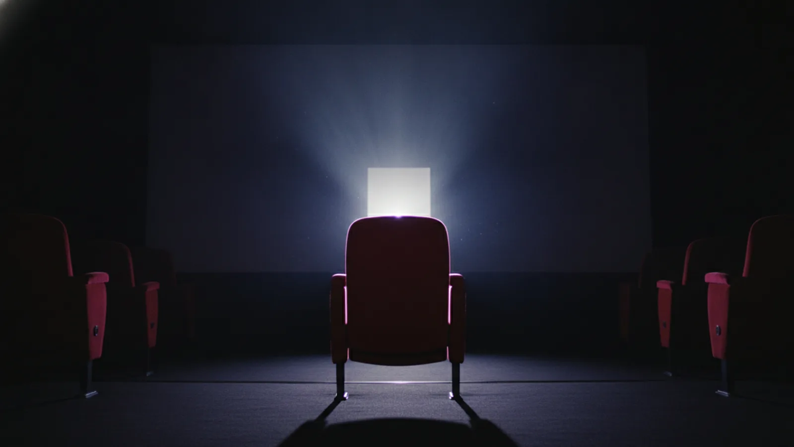 An empty cinema seat as a new projector beam lights up the dark screen